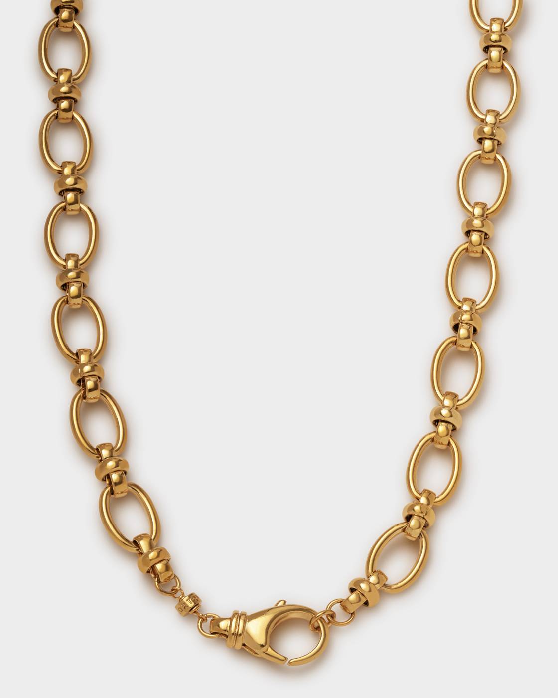 A gold-tone chain necklace with elongated oval links and smaller connecting beads, shown against a light gray background.