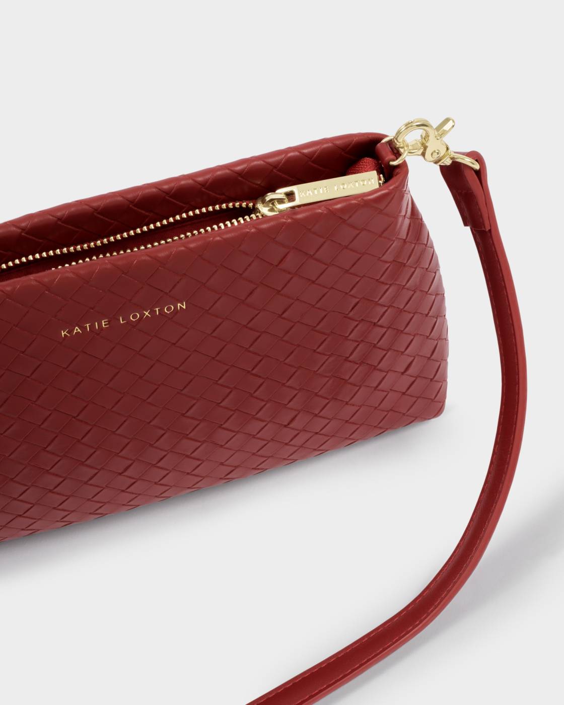 A close-up of a red woven leather wristlet clutch by Katie Loxton, featuring a gold-tone zipper, gold hardware, and a matching red wrist strap on a light gray background.