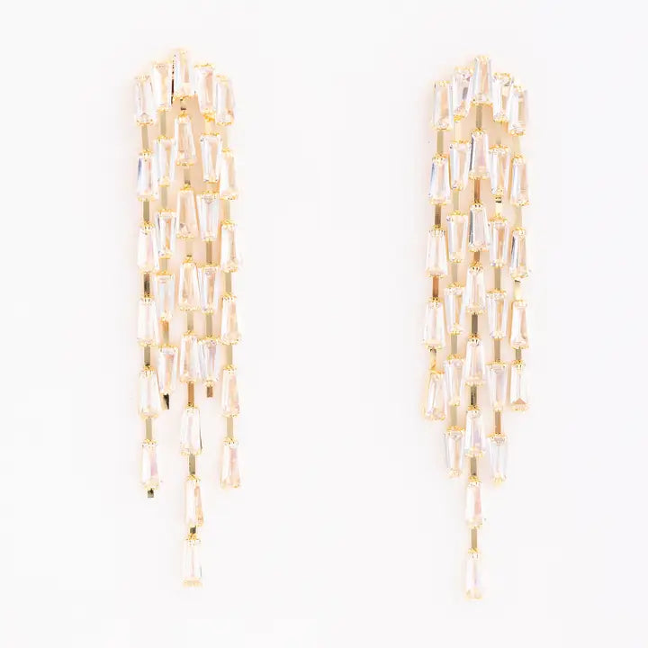 A pair of gold-toned statement earrings featuring multiple cascading strands of faceted clear baguette and teardrop crystals on a plain white background. Michelle McDowell Kennedy Earrings