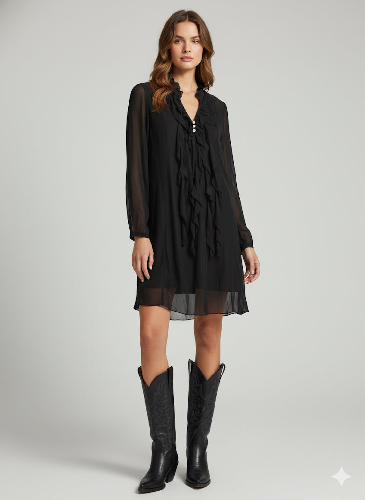 Woman wearing a black dress with sheer sleeves and a slit, paired with black cowboy boots on a gray background.