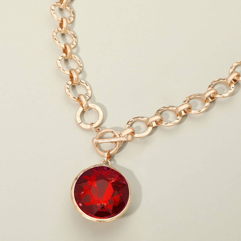 Gold chain necklace with a red gemstone pendant on a light green background