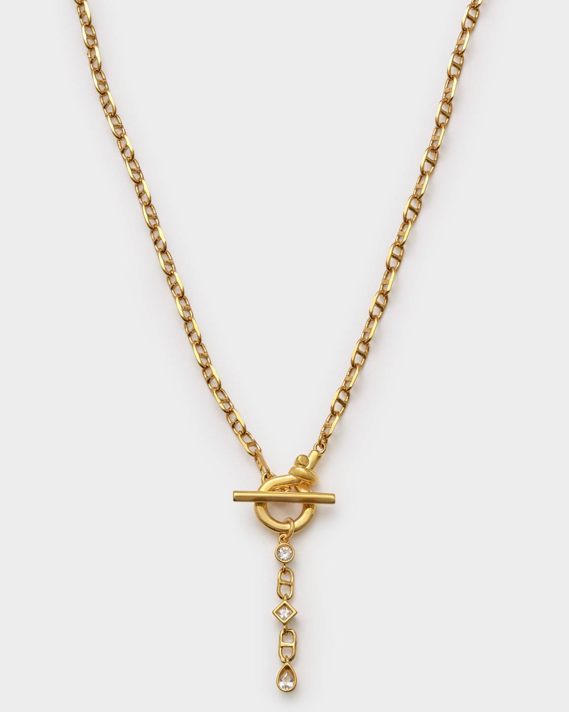 A gold chain necklace with a toggle clasp pendant and a dangling geometric charm set with clear stones, shown against a light gray background.